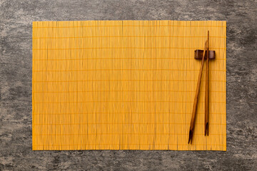 Wall Mural - Two chopsticks and bamboo mat on cement background. Top view, copy space