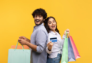 Wall Mural - Portrait of excited indian family holding shopping bags and credit card over yellow studio background