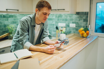 Redhead man using smartphone and a credit card in the kitchen at home