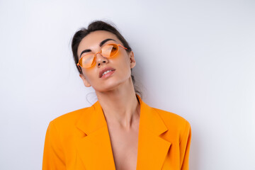 Wall Mural - Young woman in trendy stylish glasses and a bright orange oversized jacket on a white background