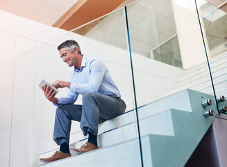 Canvas Print - Keeping his business network close to him. Shot of a mature businessman using a digital tablet on the stairs in a modern office.