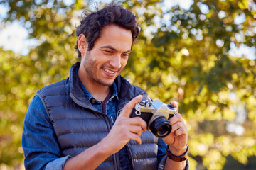 Wall Mural - Mature Man In Autumn Countryside Taking Photo On Retro Style Digital Camera To Post To Social Media