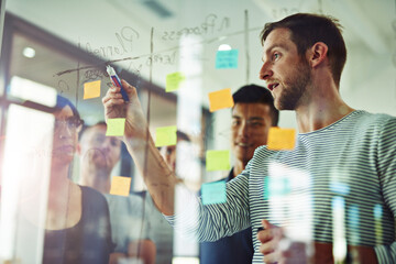 Planning is the first step. Cropped shot of a group of young designers planning on a glass board.