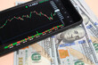 © freeman83 - Stock exchange chart on smartphone screen and hundred dollar bills on beige background.