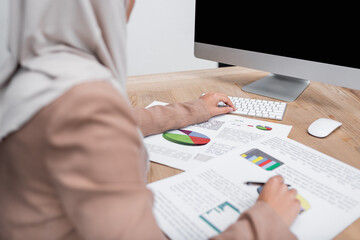 Wall Mural - partial view of blurred muslim woman working with infographics and computer at home.