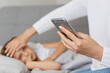 © sementsova321 - Horizontal shot of sick little girl with high temperature, having fever, suffering headache, faceless sitting near kid with cell phone in hands and calling doctor.