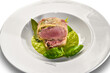 Baked pork fillet poached with bacon on pea cream with basil leaves in white plate on white
