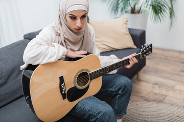 Wall Mural - muslim woman with acoustic guitar sitting on couch at home.