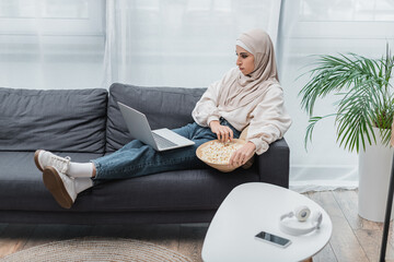 Wall Mural - mulsim woman in casual clothes and hijab watching film on laptop in living room.