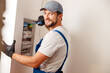 © Kostiantyn - Electrical technician in uniform smiling at camera, using screwdriver while checking fuses in a switchboard on the wall