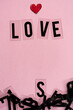 letras formando la palabra LOVE con un corazón de papel rojo sobre fondo rosado y letras desordenadas debajo en vertical