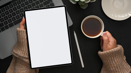 A female using tablet computer and sipping hot coffee. top view