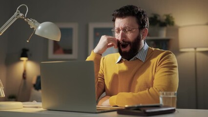 Man yawns, boredom emotion. Tired sleepy bored man with glasses in home office looking at computer screen and yawns for long time
