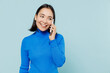 © ViDi Studio - Fun young woman of Asian ethnicity 20s years old wears blue shirt hold in hand talk on mobile cell phone conducting pleasant conversation isolated on plain pastel light blue background studio portrait