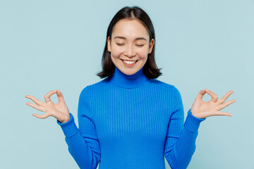 Wall Mural - Young woman of Asian ethnicity 20s years old wear blue shirt hold spreading hands in yoga om aum gesture relax meditate try to calm down isolated on plain pastel light blue background studio portrait