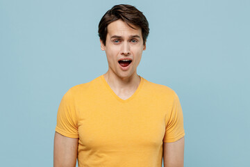 Young displeased sad disappointed man 20s wear yellow blank print design t-shirt look camera with open mouth isolated on plain pastel light blue background studio portrait. People lifestyle concept.