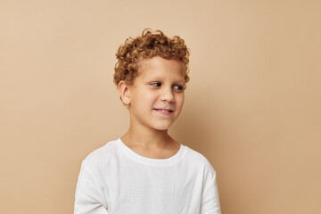 Wall Mural - Cheerful boy with curly hair in a white t-shirt beige background