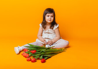 Wall Mural - cute little blonde girl with a bouquet of tulips in a cotton dress on a pink background. March 8