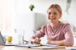 © Prostock-studio - Smiling european adolescent girl blonde pupil study at home at table with laptop in light kitchen interior