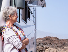 Portrait Of Beautiful Smiling Senior Caucasian Woman With Glasses Traveling In Motor Home Camper Standing Outdoor Looking Away At Landscape. Carefree Woman Enjoying Free Lifestyle, Vacation, Travel