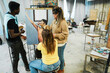 © DisobeyArt - Mature teacher working with art students during painting class at school - Focus on woman face