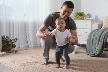 Wall Mural - Father supporting his baby daughter while she learning to walk at home