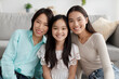 © Prostock-studio - Positive multi generation Asian family posing and smiling at camera, sitting on floor in living room