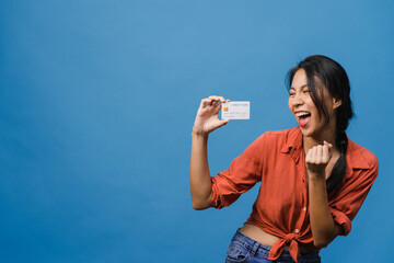 Wall Mural - Young Asia lady show credit bank card with positive expression, smiles broadly, dressed in casual clothing feeling happiness and stand isolated on blue background. Facial expression concept.