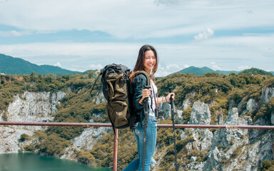 Asian beautiful woman wearing hat and casual clothes, smiling with happiness, adventure traveling alone and hiking on the top of mountains with backpack in summer vacation trip on weekend.