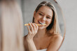 Oral hygiene, healthy teeth and care. Young woman brushing teeth with toothbrush and looking in mirror in bathroom