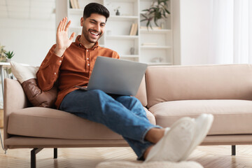 Wall Mural - Smiling man working on laptop waving hand