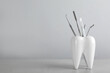 Tooth shaped holder with dentist's tools on light grey table. Space for text