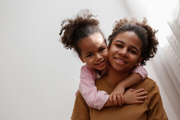 Younger and older sister spending time together at home. Two black girls of different age hugging and showing affection. Black female siblings having fun and bonding. Background, copy space, close up.