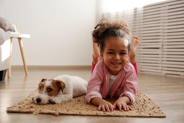 Little black girl playing with her friend, the adorable wire haired Jack Russel terrier puppy at home. Preschooler with rough coated pup lying on the floor. Interior background, close up, copy space.