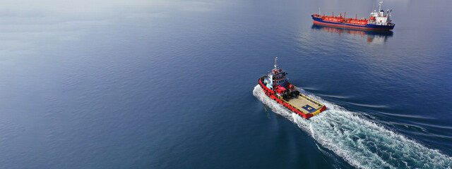 Aerial drone ultra wide photo of industrial tug assisting vessel cruising near container terminal port