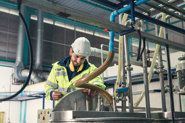 Caucasian technician engineer man in uniform with tablet checking and control boiler tanks and liquid pipeline in production line at factory