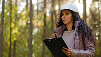 millennial female technician ecologist looking up at treetops, young indian woman in hardhat with cl