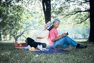 Wall Mural - Asian elderly couple, attractive wife and husband, picnic and relaxing on the green lawn in garden, are smile and happy together, to relationship of retirement age and nature concept.