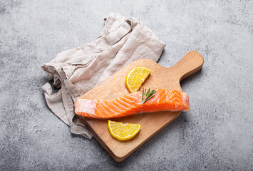 Wall Mural - Raw salmon fish fillet with lemon wedges and rosemary on wooden cutting board on gray stone concrete rustic background kitchen table from above, healthy eating and diet 