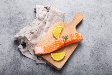 Wall Mural - Raw salmon fish fillet with lemon wedges and rosemary on wooden cutting board on gray stone concrete rustic background kitchen table from above, healthy eating and diet 