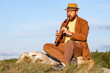 adult bearded man closing his eyes plays the flute while sitting in nature