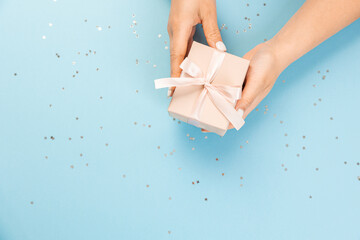 Wall Mural - A hand holds a blue gift box on a blue background with glitter stars. top view, copy space