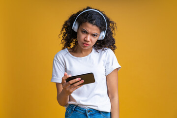 Wall Mural - Portrait of frowning girl holding smartphone in hand and looking at the camera with sullen face expression feeling frustrated that she lost online play tournament