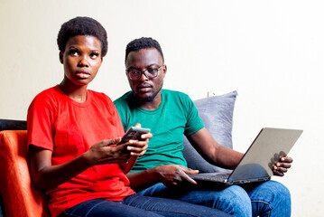 Poster - young couple sitting together on a sofa at home.