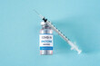 View from above vial with new coronavirus vaccine Omicron variant and syringe on blue light background, flat lay. Copy space for text