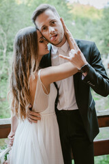 Wall Mural - Portrait of a bride touching the groom's face with sensuality and love as he shows the rock sign and tongue to the camera. The concept of facial expressions and