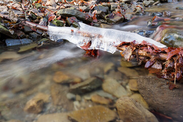 Sticker - Ice on a branch above the surface of a flowing river.