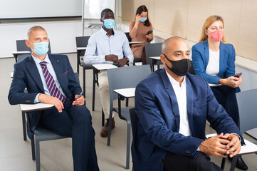 Wall Mural - International group of business people wearing protective face masks listening to presentation in conference room. Concept of precautions and social distancing in COVID 19 pandemic..