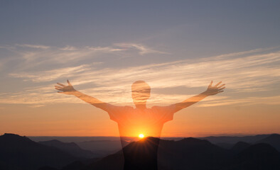 Man with arms raised with sunset in the mountains in the background. Person worshiping or thanking God. Success and happiness concept.