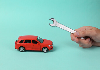 Hand holds wrench in front of toy car model on blue background. Repair, auto workshop